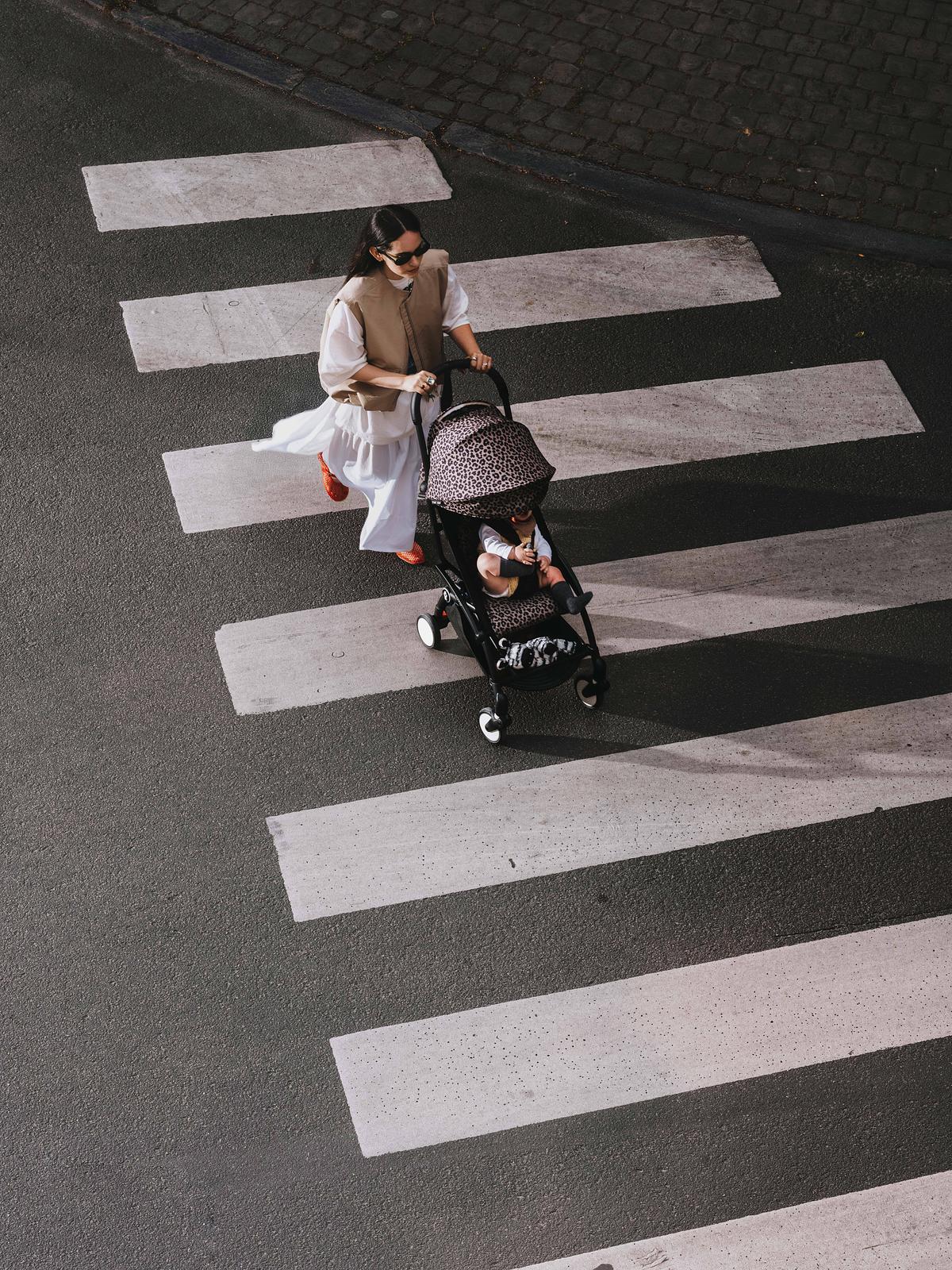 Une femme pousse un bébé dans une poussette STOKKE YOYO sur un passage piéton.