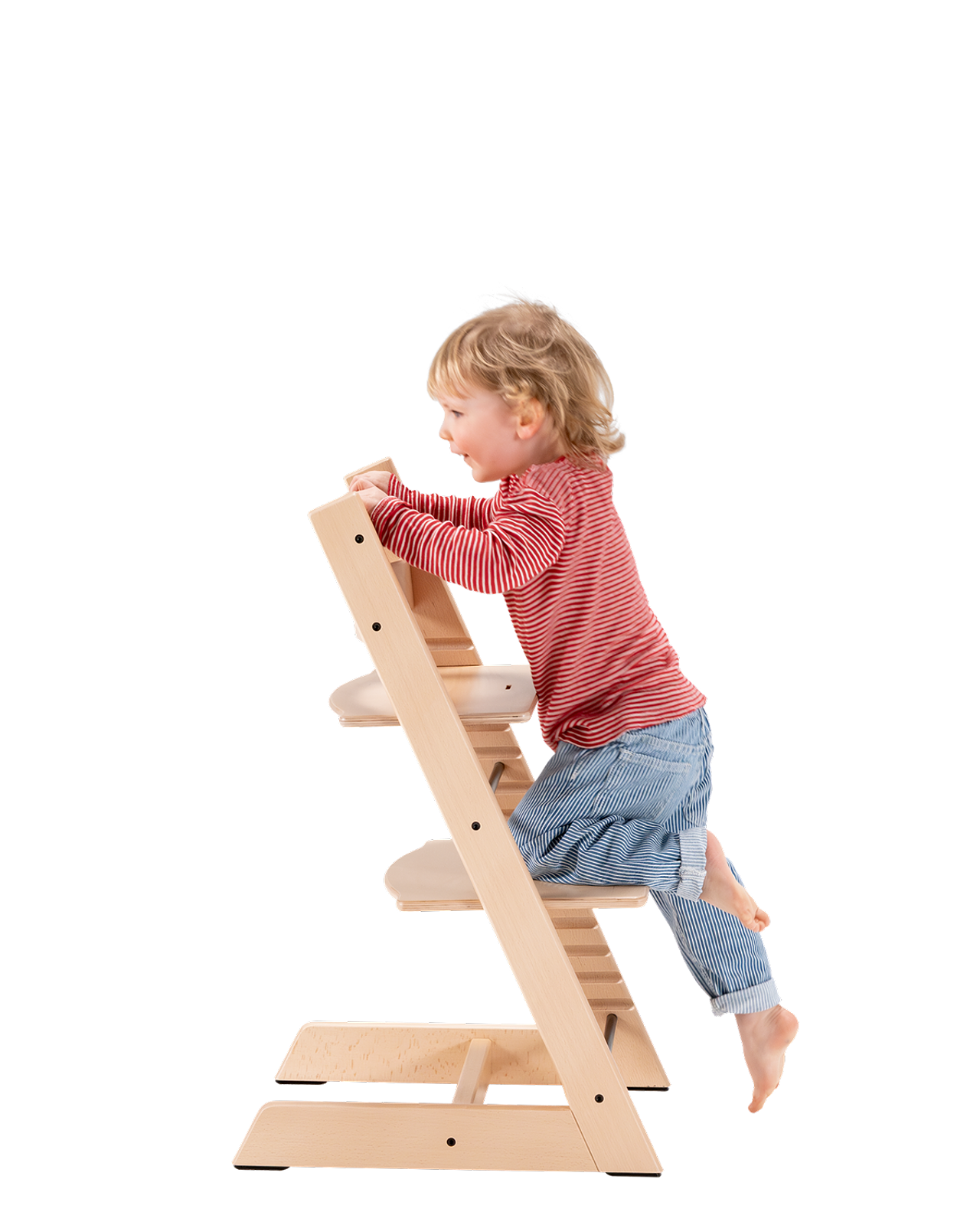 Un bambino biondo si arrampica su una sedia Tripp Trapp in legno chiaro.