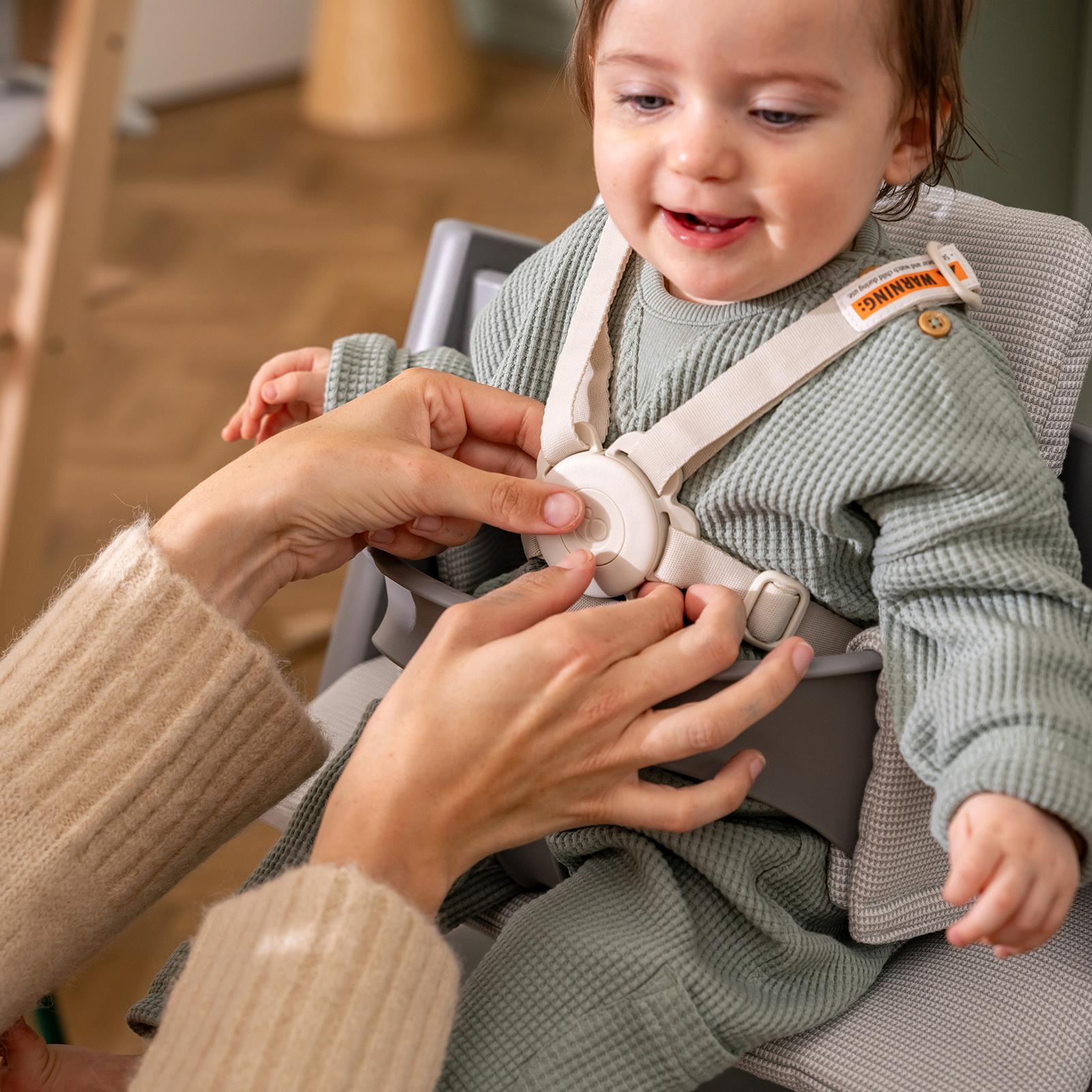 Un bambino sorridente in un seggiolone Tripp Trapp mentre le mani allacciano l'imbracatura.