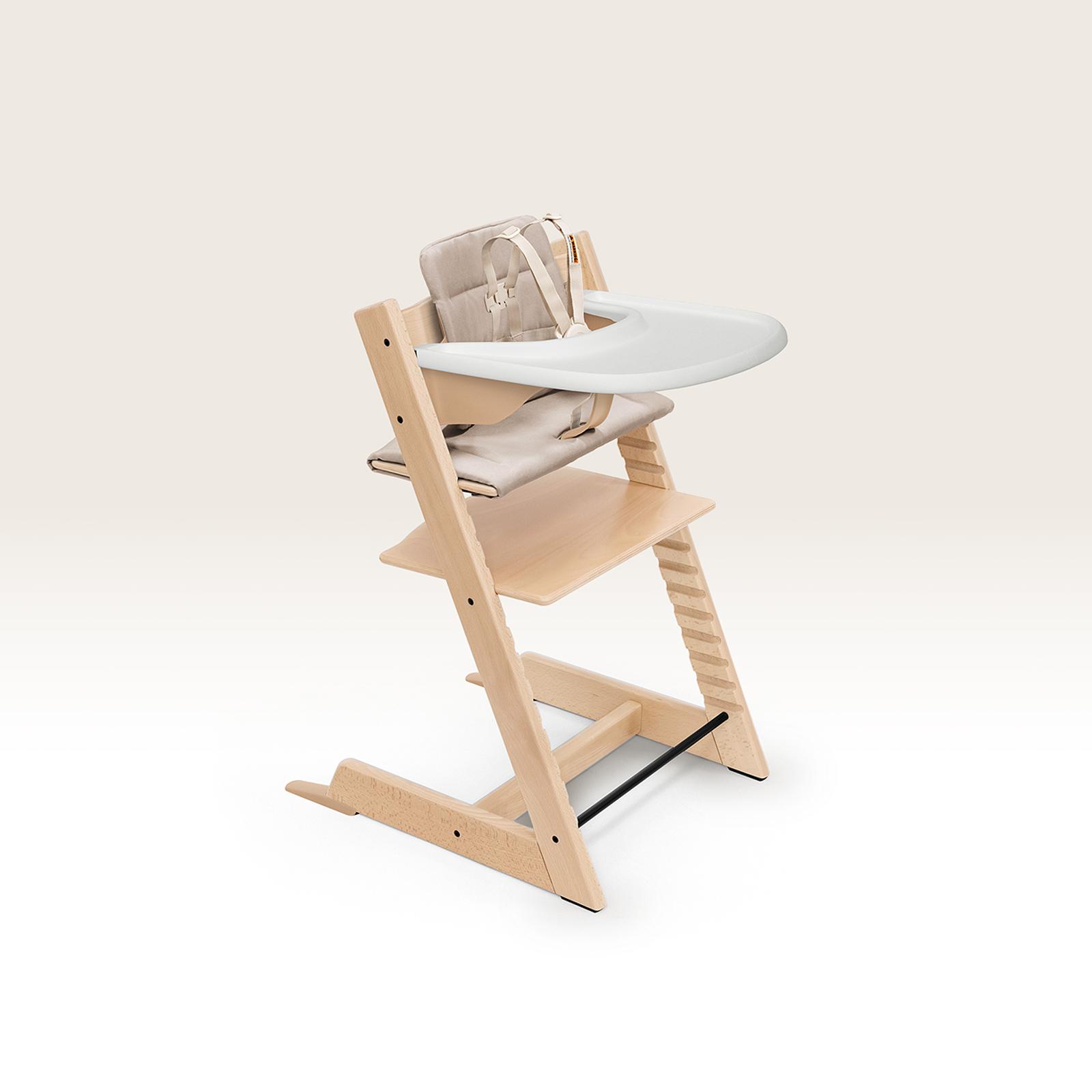 Un seggiolone Tripp Trapp con un vassoio bianco e cuscini beige.