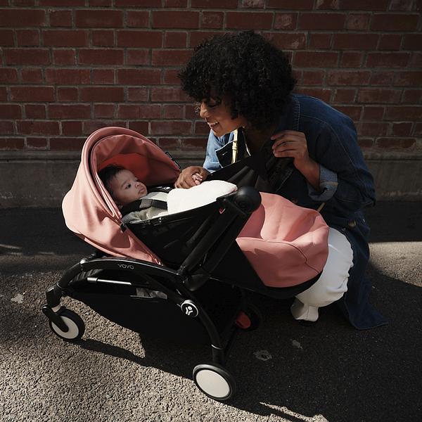 Femme souriant à un bébé dans une poussette rose Stokke YOYO.