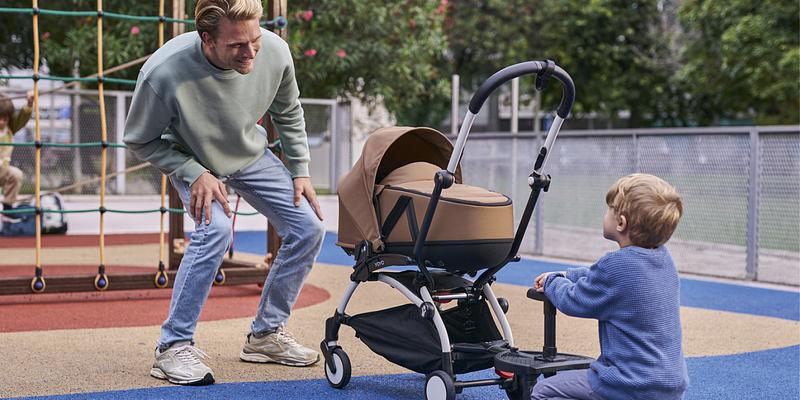 A dad and his son at a playground, standing next to a YOYO stroller with bassinet