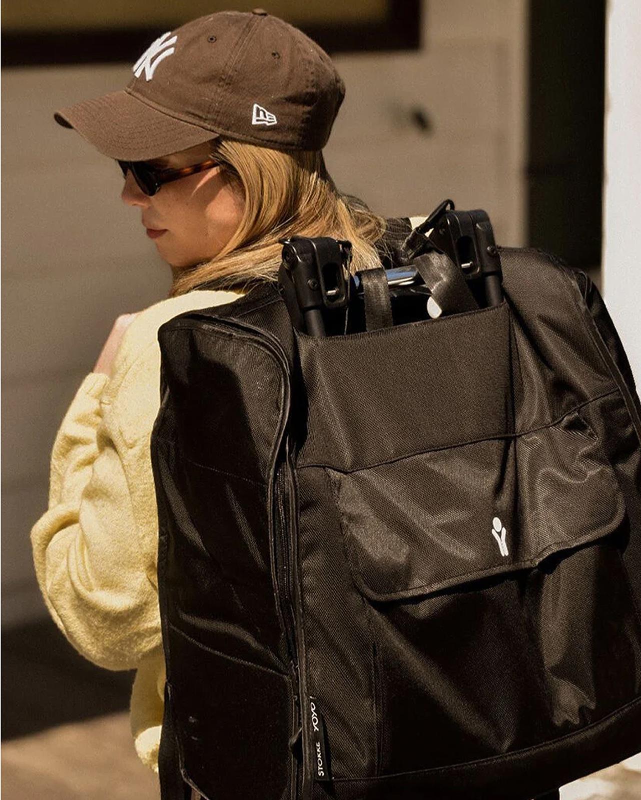 Femme blonde portant une casquette des Yankees, transportant une poussette STOKKE YOYO dans un sac de voyage noir.