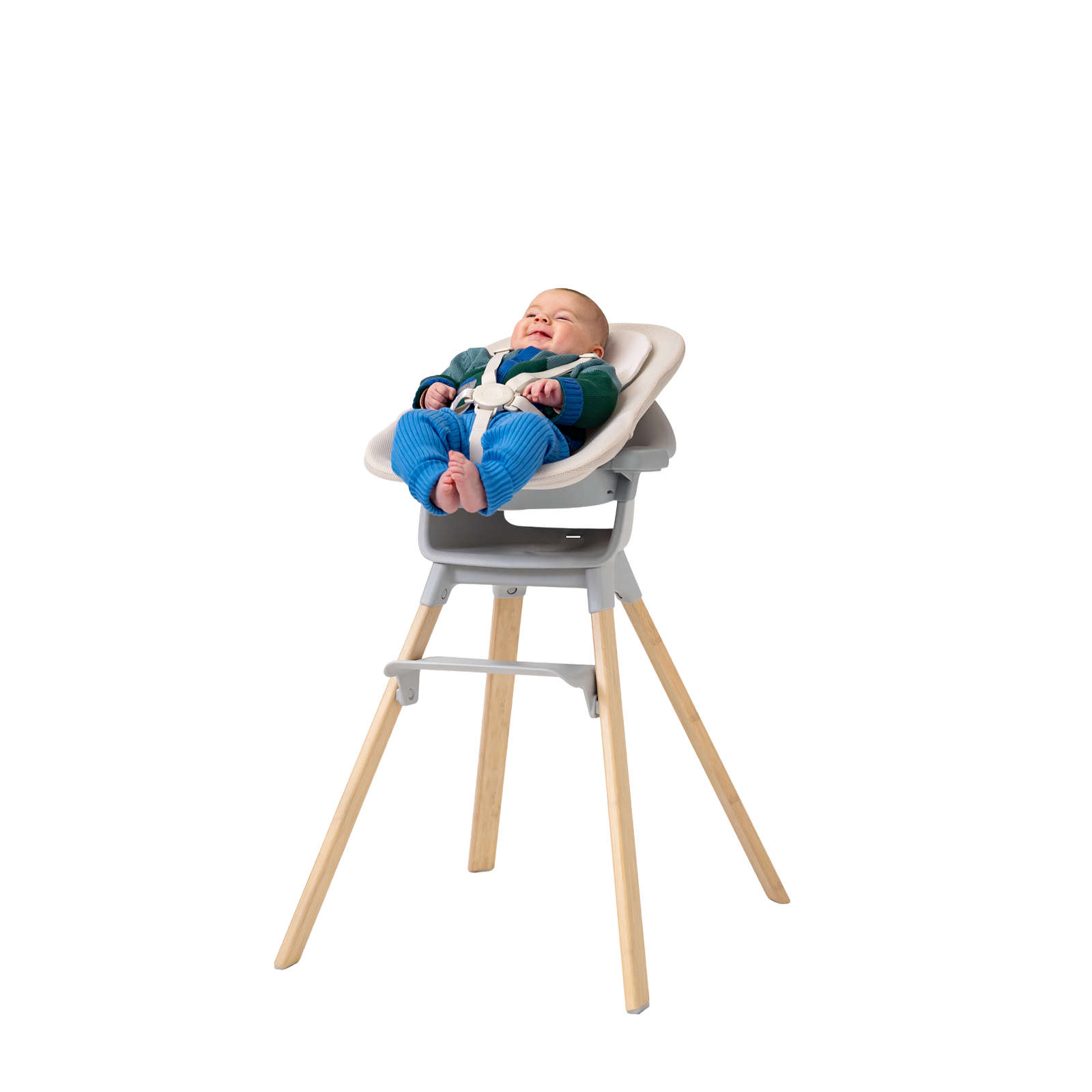Ein lächelndes Baby lehnt sich in einem grauen Hochstuhl mit cremefarbenem Sitzeinsatz und Holzbeinen zurück.