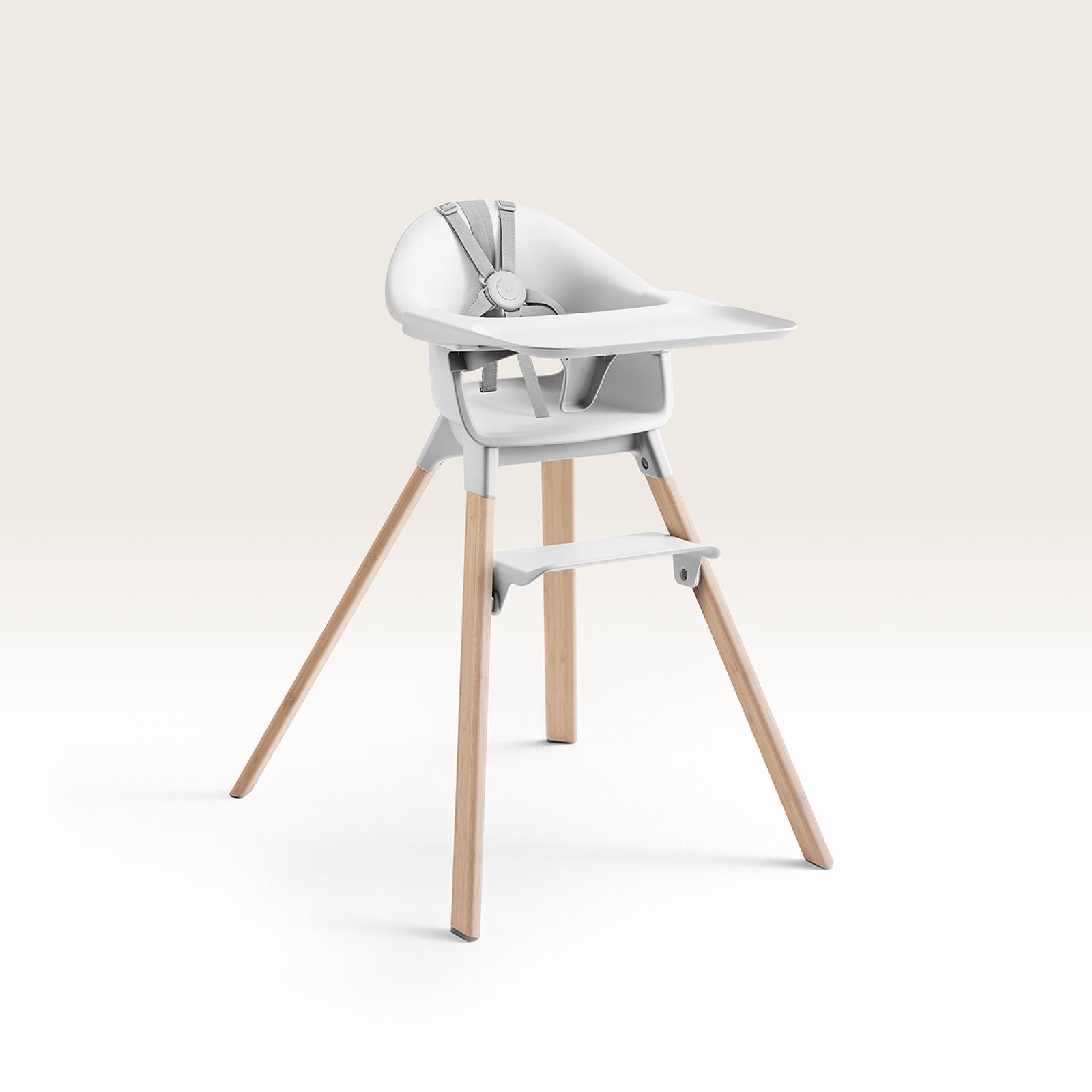 A white baby high chair with light wooden legs, a feeding tray, and a grey harness.