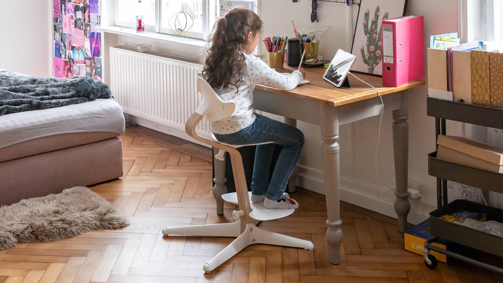 Image of a young girl sitting in her room at her desk writing in her journal in her Stokke Nomi chair.