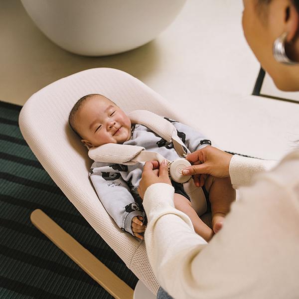Mother is securing her child in the bouncer with 5-point harness