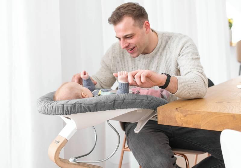 Dad looking down at newborn baby laying in Stokke® Nomi® chair with newborn set.