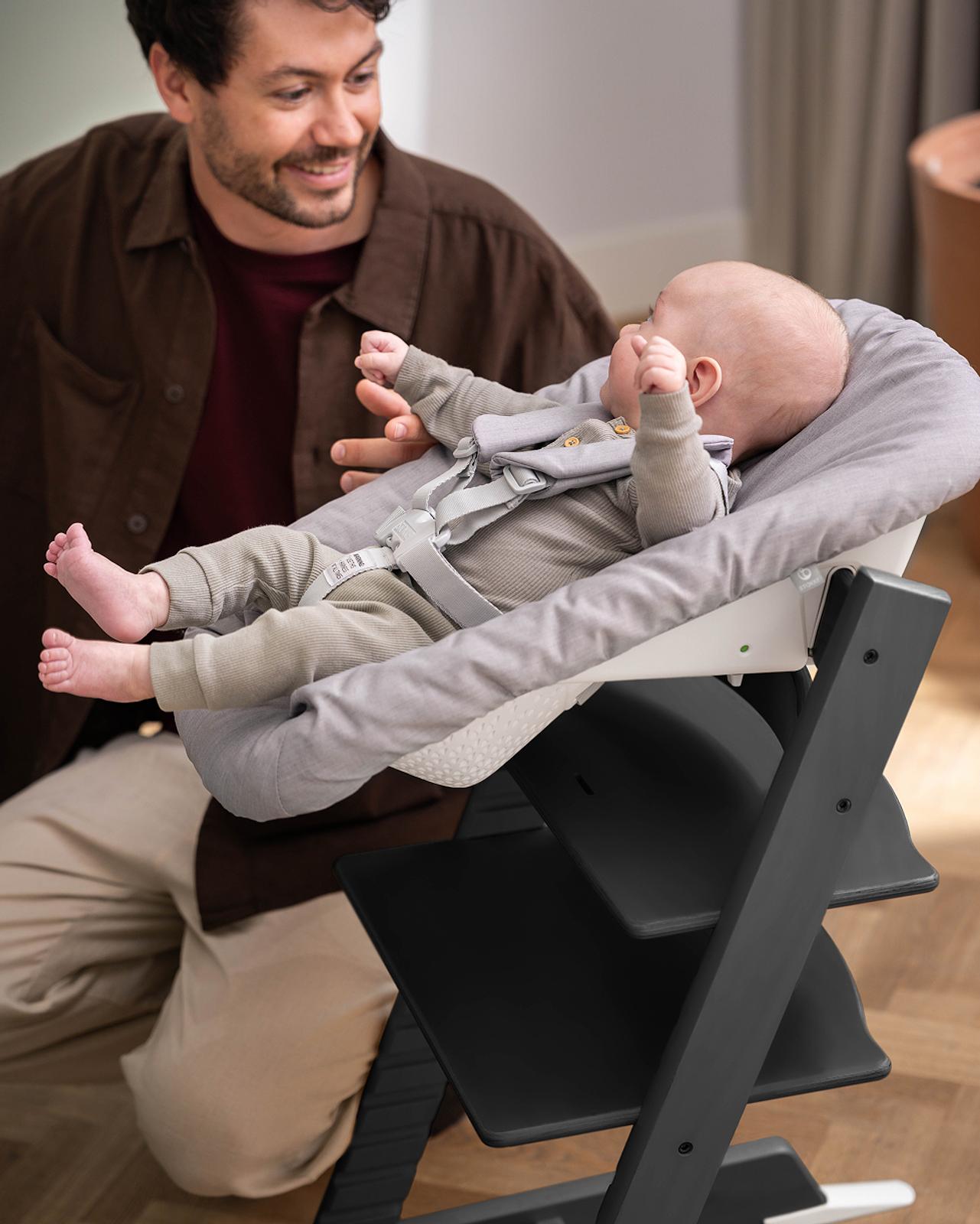 Un hombre sonríe a un bebé en una trona Tripp Trapp con un Newborn Set.