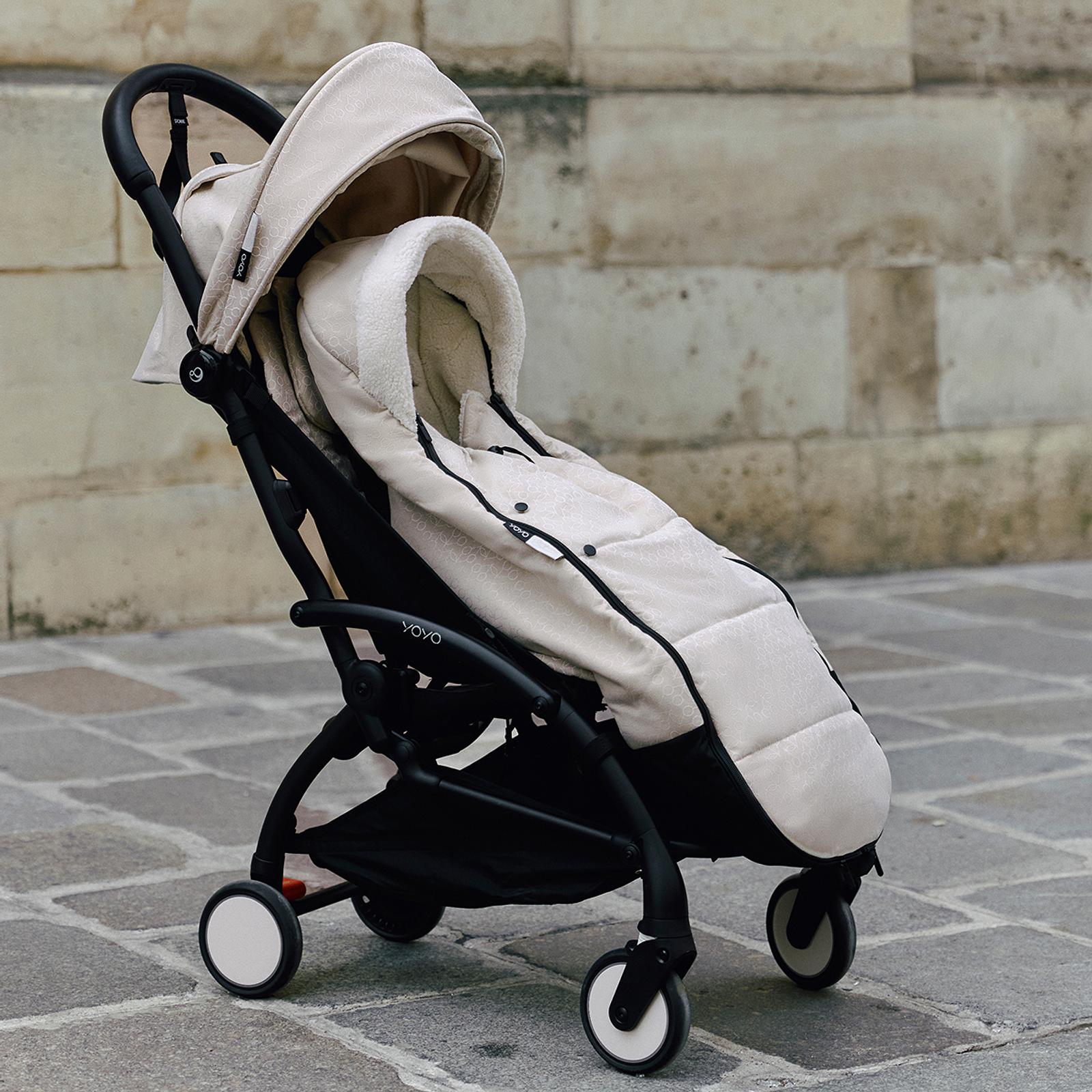 STOKKE YOYO stroller with beige canopy and plush footmuff on a cobblestone street.