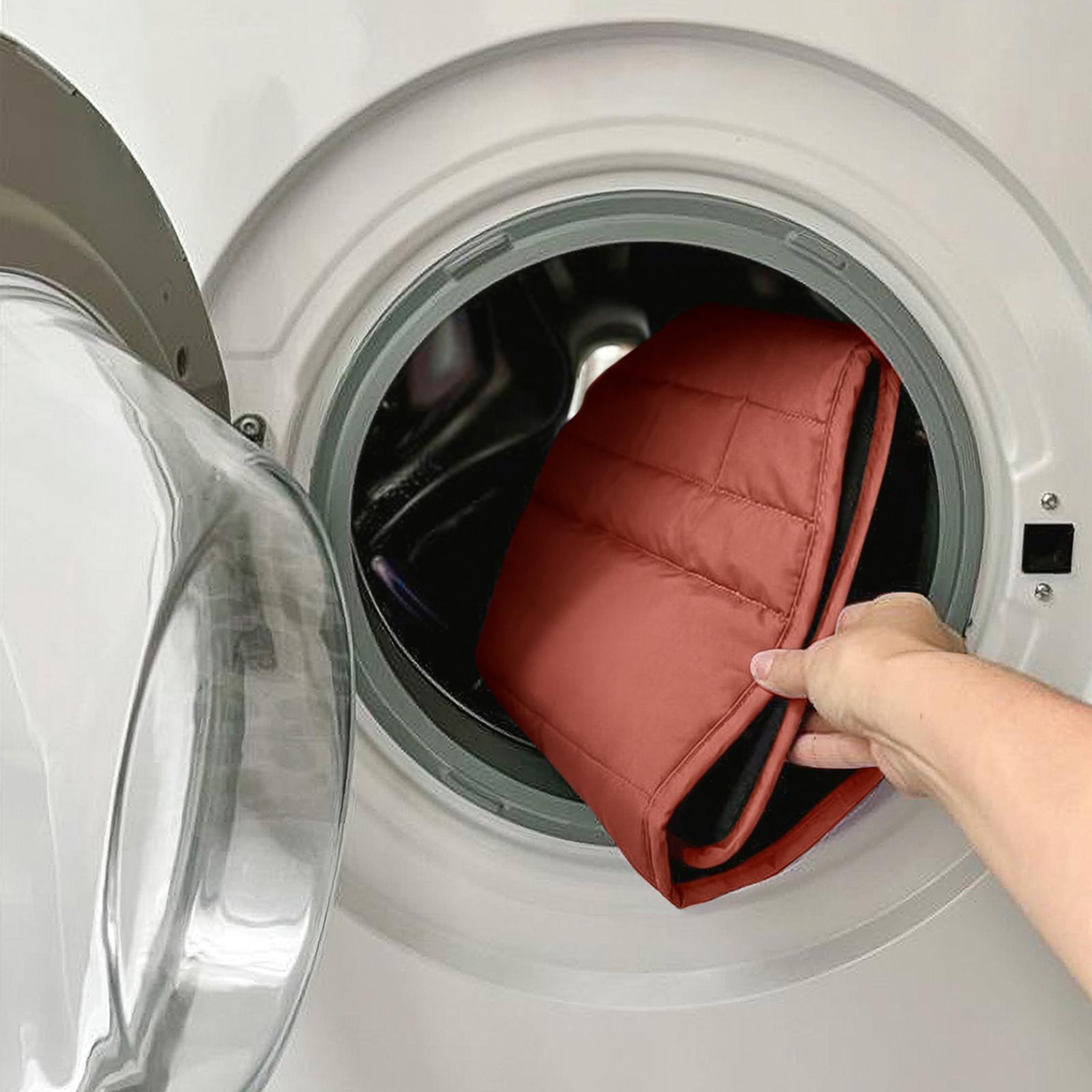 A hand puts a reddish-brown quilted seat liner into a washing machine.