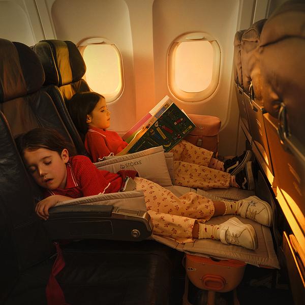 Young child is sleeping on the airplane while laying on JetKids children's luggage.