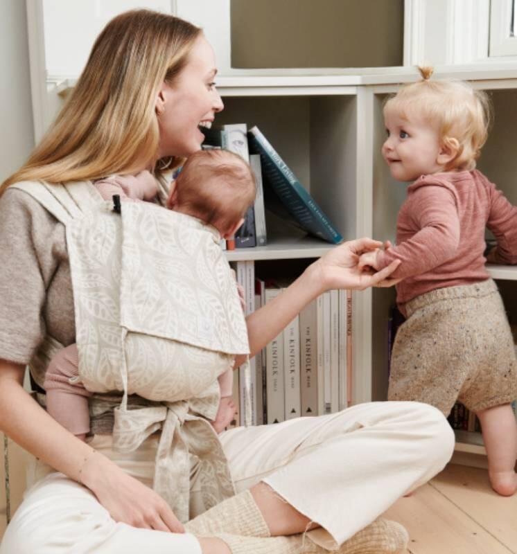 Mom playing with her toddler while newborn is in the Limas™ Carrier. 