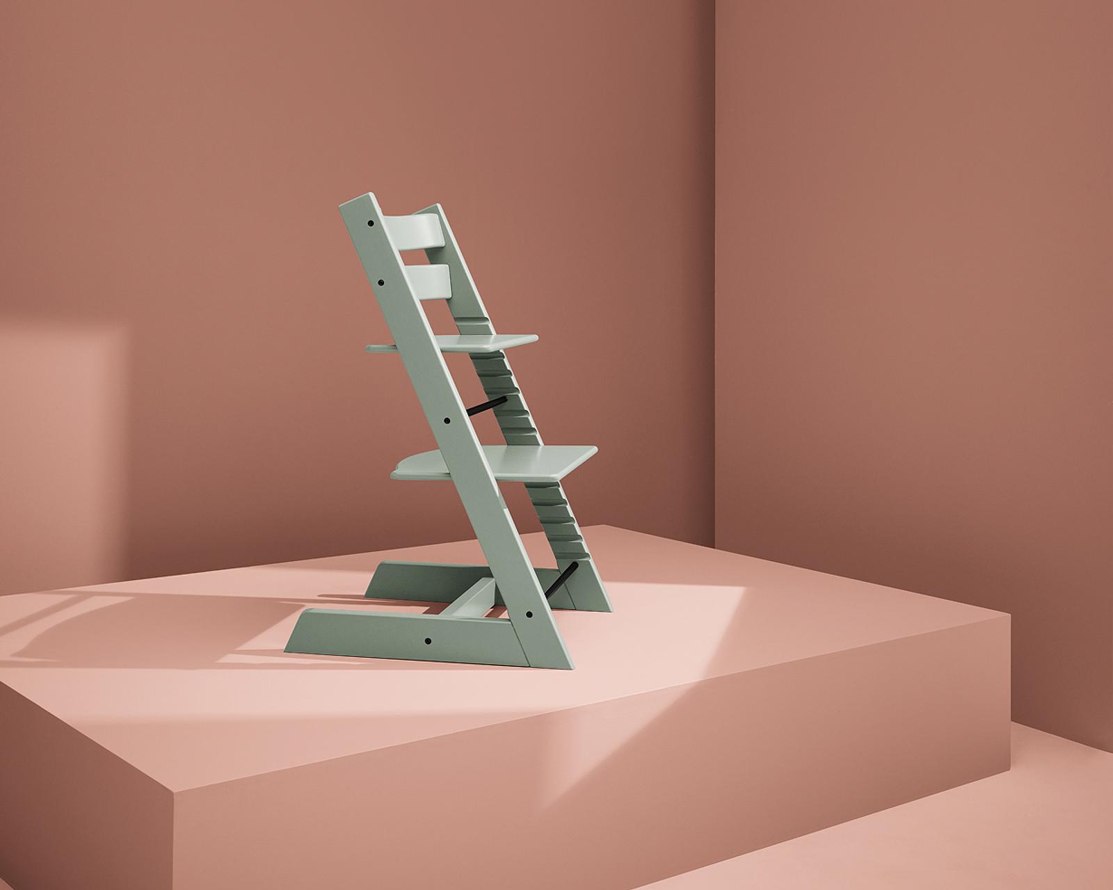 En mintgrön Tripp Trapp-stol står på en rosa geometrisk plattform mot en rosa vägg.