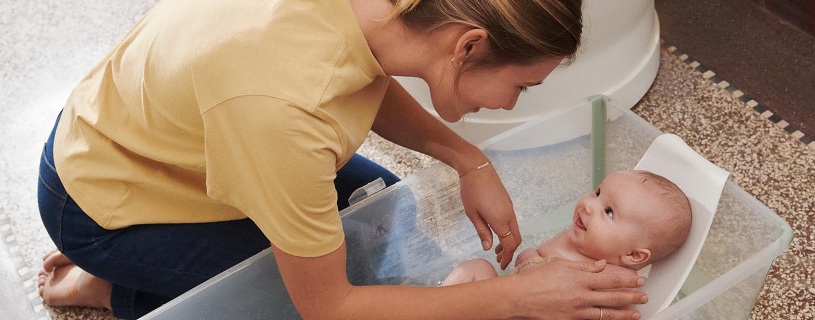 A mother looking at her baby in Flexi bath in color transparent green with newborn support.