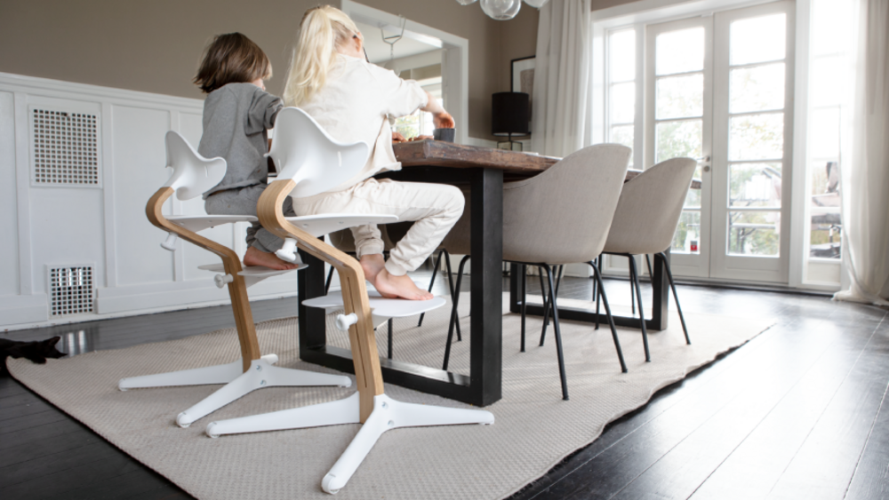 Two children sitting at the dining table on Stokke® Nomi® chairs.