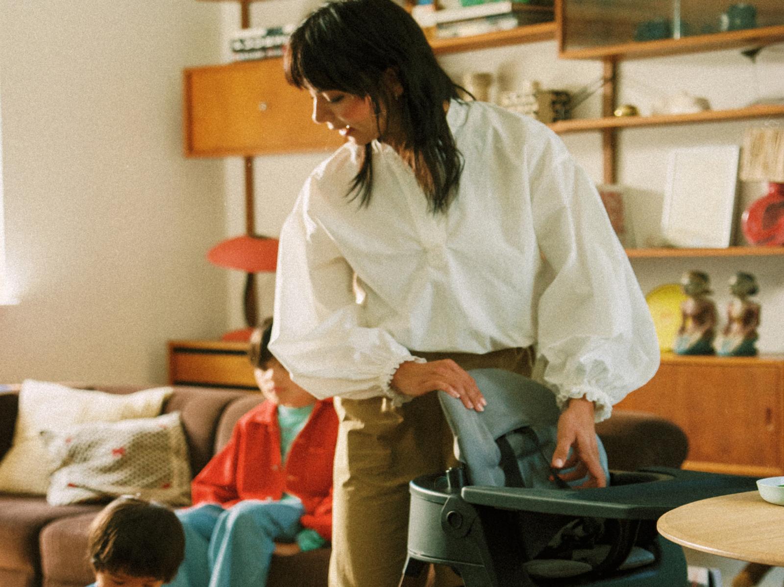 Woman adjusts a dark grey Tripp Trapp high chair in a living room.