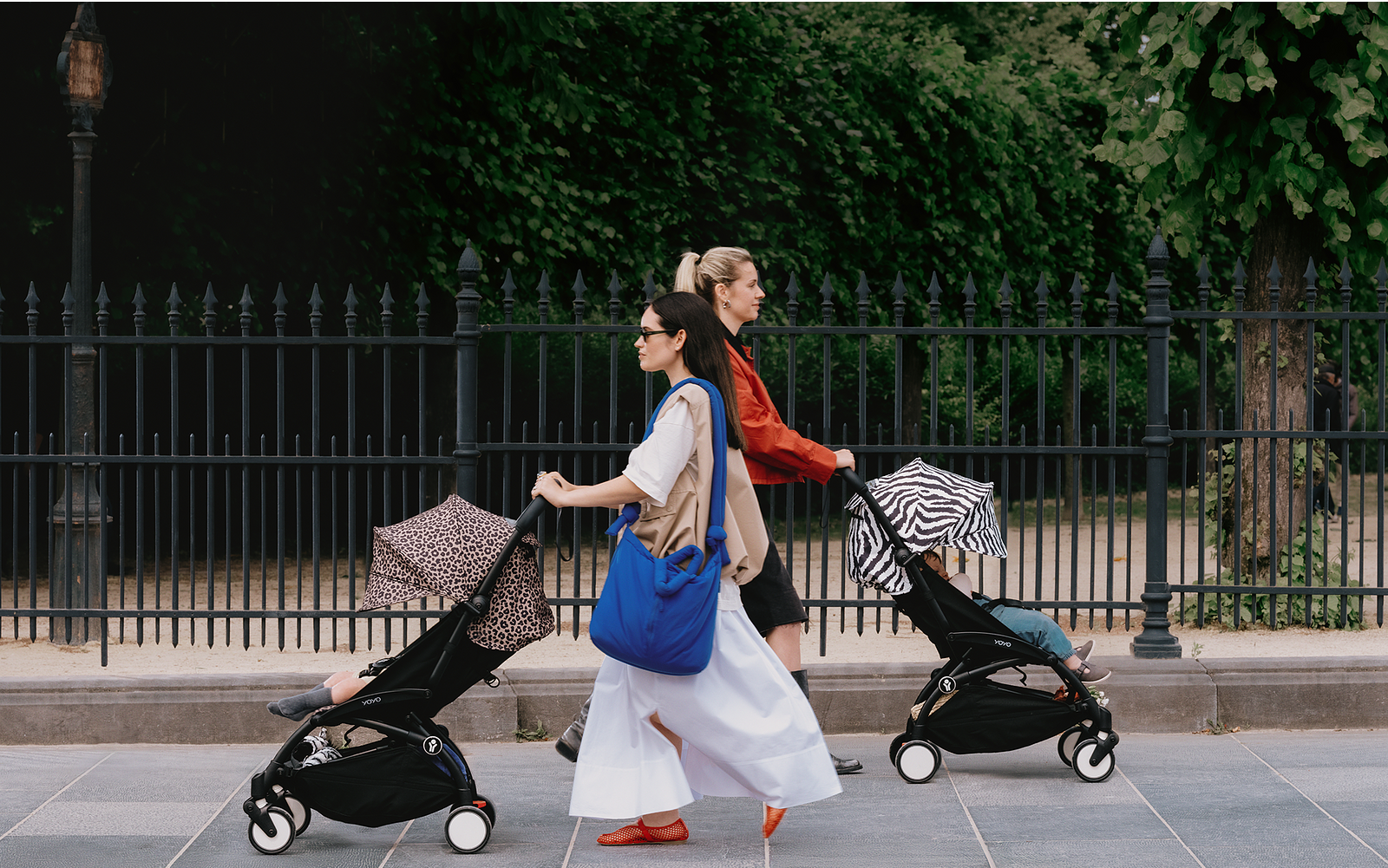 Two women push YOYO strollers with leopard and zebra print canopies outdoors.