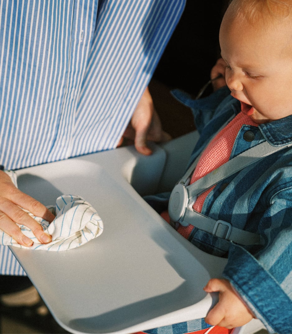 Adult hand cleaning high chair tray with cloth